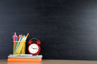 Kara tahta arka planda kırmızı çalar saat ile okul malzemeleri