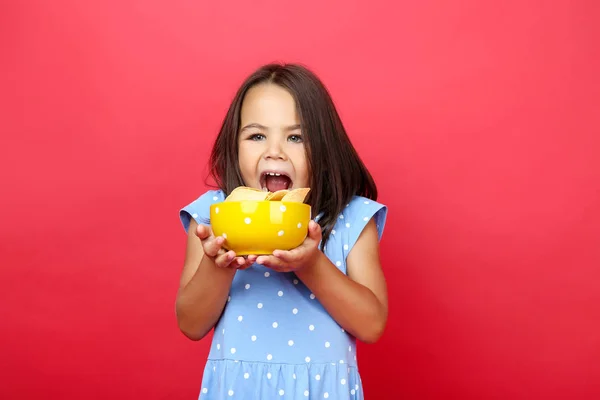 Gadis kecil yang cantik dengan keripik kentang dalam mangkuk di backgroun merah — Stok Foto