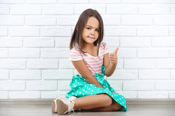 Красива маленька дівчинка показує великий палець на білій цегляній стіні backg — стокове фото