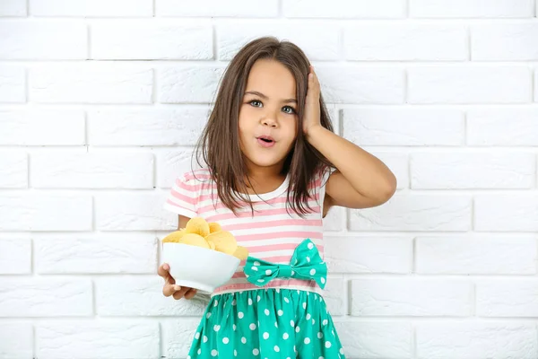 Gadis kecil yang cantik dengan keripik kentang dalam mangkuk di bata putih w — Stok Foto