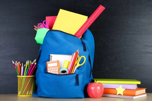 Material escolar con mochila azul sobre fondo pizarra —  Fotos de Stock