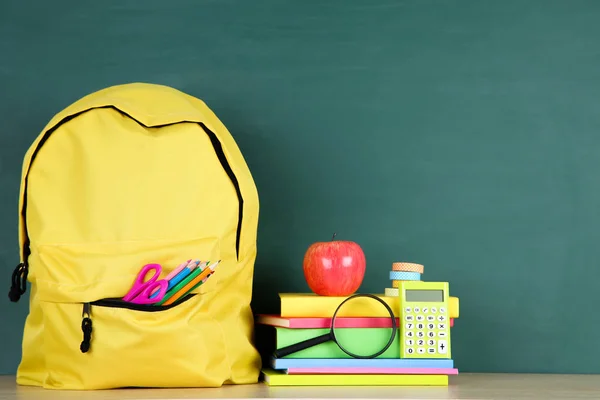 Material escolar con mochila amarilla sobre fondo de pizarra —  Fotos de Stock