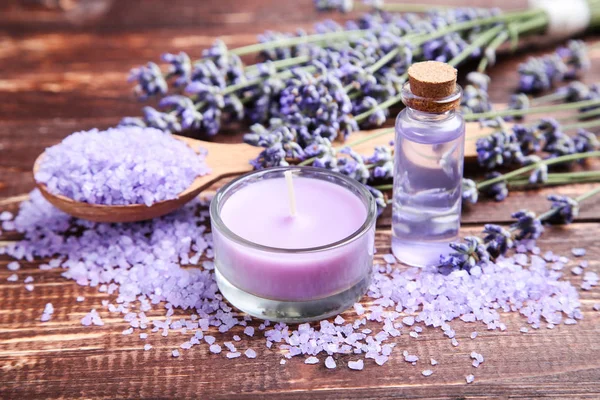 Lavender oil in bottle with flowers, salt and candle on brown wo — Stock Photo, Image