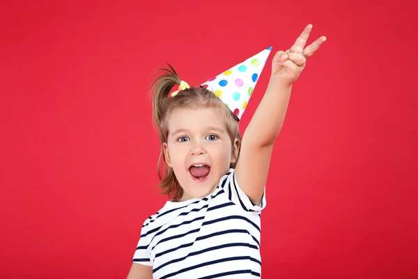 Linda niña en gorra de cumpleaños sobre fondo rojo — Foto de Stock