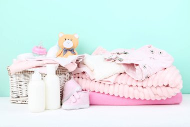 Şişeli bebek kıyafetleri ve mavi arka planda yumuşak ayı oyuncağı.