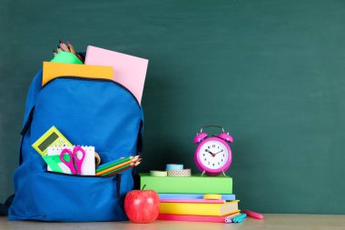 Kara tahta arka planda mavi sırt çantası ile okul malzemeleri