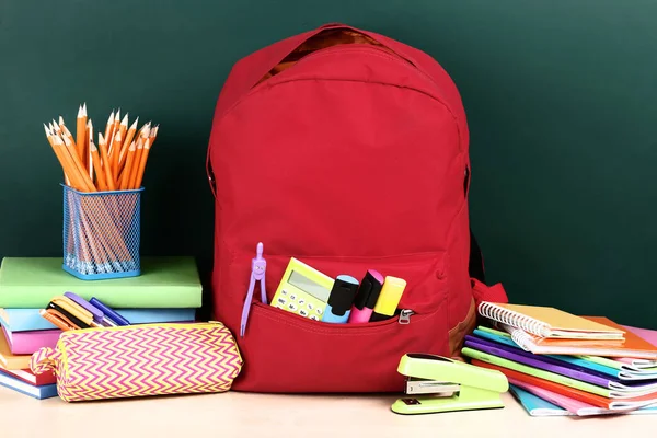 Mochila con útiles escolares sobre fondo verde —  Fotos de Stock