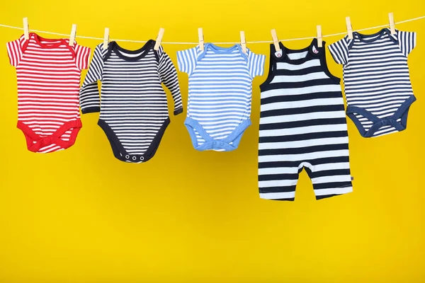 Ropa de bebé colgada sobre fondo amarillo —  Fotos de Stock