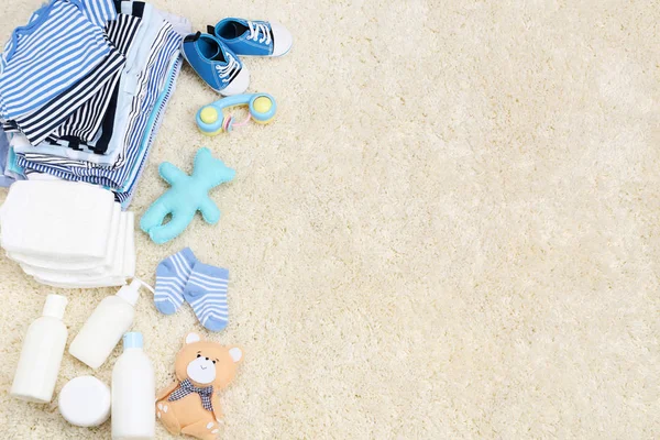 Bebek kıyafetleri ve halı üzerinde bebek bezi.