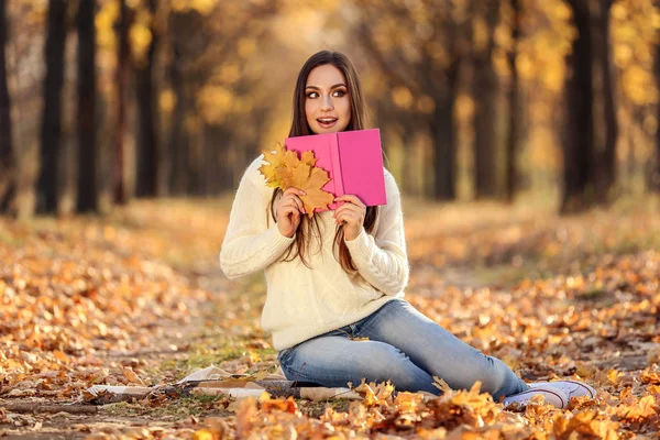Güzel kadın kuru yapraklar ve kitap sonbahar parkta oturan