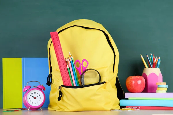 Material escolar con mochila amarilla sobre fondo de pizarra — Foto de Stock