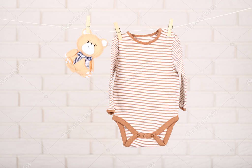 Baby bodysuit and soft toy hanging on brick wall background