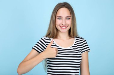 Güzel genç kadın mavi arka plan üzerinde başparmak gösteren