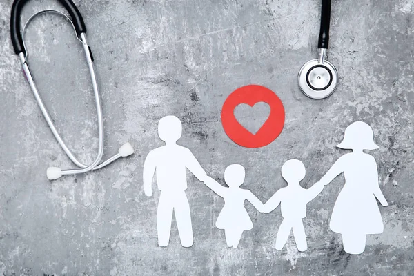 Семейные фигуры с красным сердцем и стетоскопом на сером фоне — стоковое фото