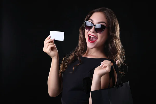 Joven mujer sosteniendo tarjeta de crédito y bolsa de compras sobre fondo negro — Foto de Stock