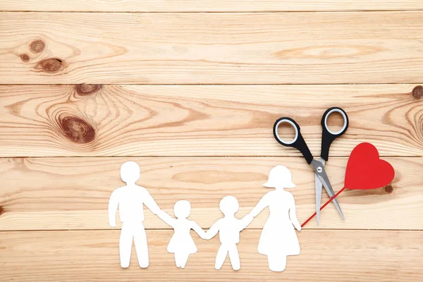 Семейные фигуры с ножницами и красным сердцем на деревянном столе — стоковое фото