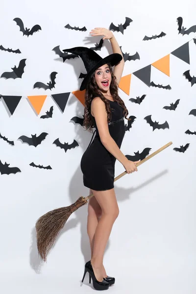 Jovem mulher em traje de Halloween com vassoura no fundo branco — Fotografia de Stock