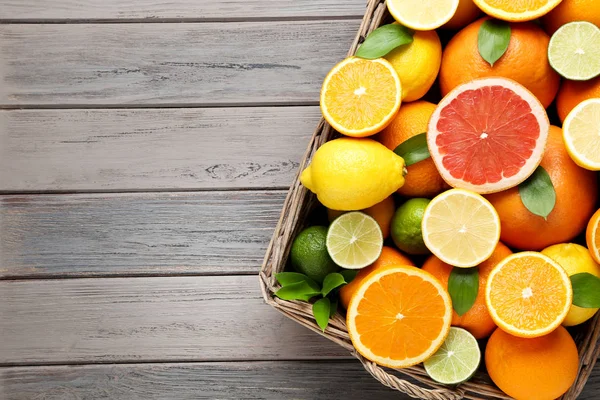 木製のテーブルの上にバスケットに緑の葉と柑橘類の果物 — ストック写真