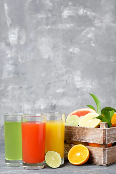 Citrus juice in glasses with fruits on grey wooden table — Stock Photo, Image