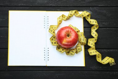 Ahşap masa üzerinde kırmızı elma ve not defteri ile ölçüm bandı