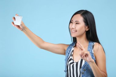 Mavi arka planda akıllı telefondan selfie çeken genç bir kadın.