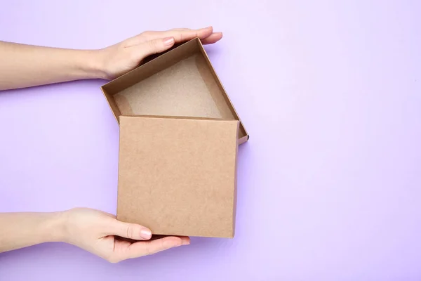 Manos femeninas abriendo caja de regalo marrón sobre fondo púrpura — Foto de Stock