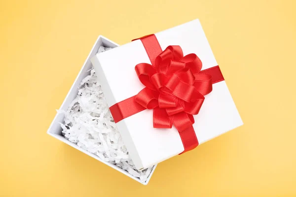 Open gift box with red bow and shredded paper on yellow backgrou