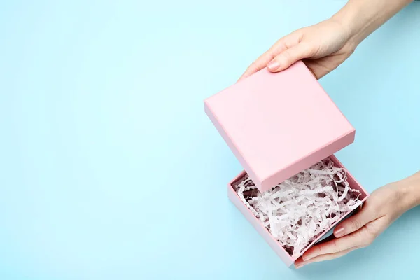 Female hands opening pink gift box with shredded paper on blue b — Stock Photo, Image