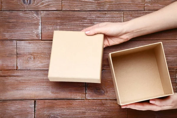 Manos femeninas abriendo caja de regalo en mesa de madera marrón — Foto de Stock