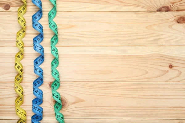 Colorful measuring tapes on brown wooden table — Stock Photo, Image