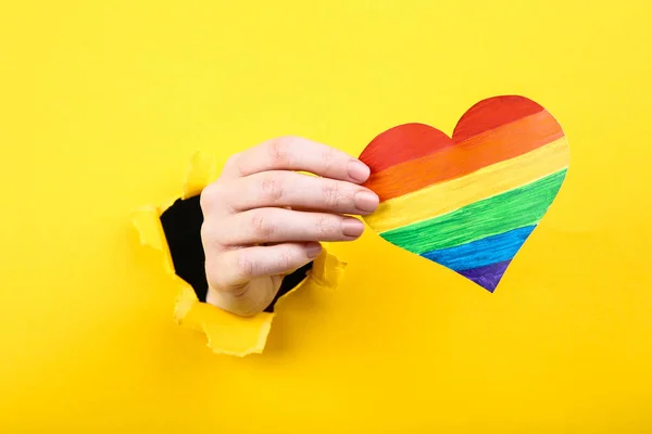 Hand holding paper rainbow heart from yellow torn paper — Stock Photo, Image