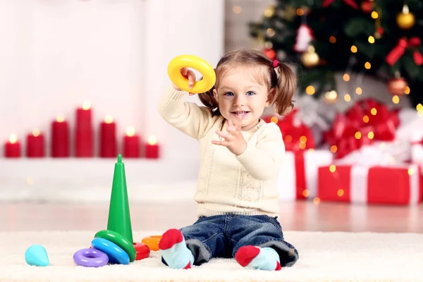 Menina com brinquedos sentados perto da árvore de natal em casa — Fotografia de Stock