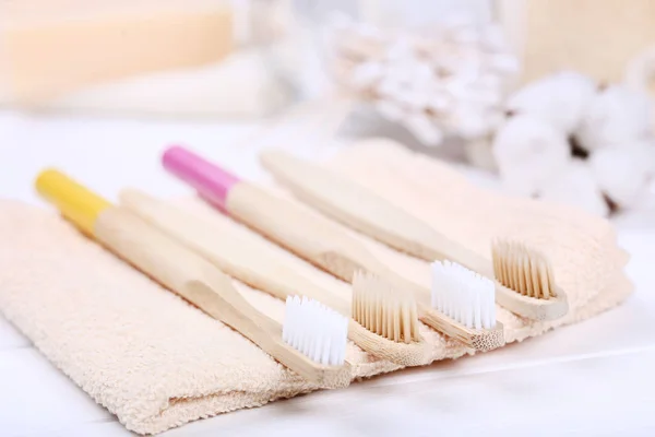 Bamboo toothbrushes with towel on white wooden table — Stock Photo, Image