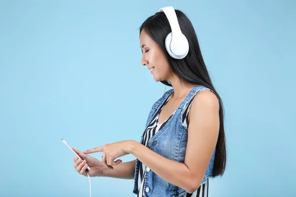 Hermosa mujer con auriculares y teléfono inteligente en el fondo azul — Foto de Stock