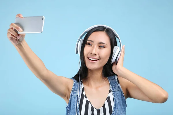 Mujer joven con auriculares haciendo selfie en el teléfono inteligente en azul — Foto de Stock