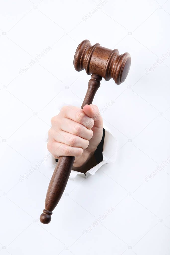 Hand holding judge gavel from white torn paper