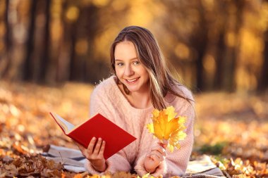 Genç güzel kız sonbahar parkta kitap ile yalan