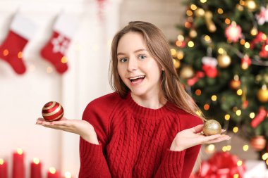 Evde yılbaşı ağacının yanında oturan baubles ile genç kız