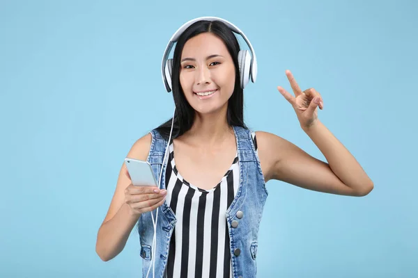 Schöne Frau mit Kopfhörer und Smartphone auf blauem Hintergrund — Stockfoto