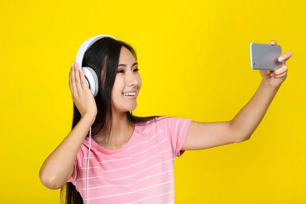 Mujer joven con auriculares haciendo selfie en el teléfono inteligente en yello — Foto de Stock