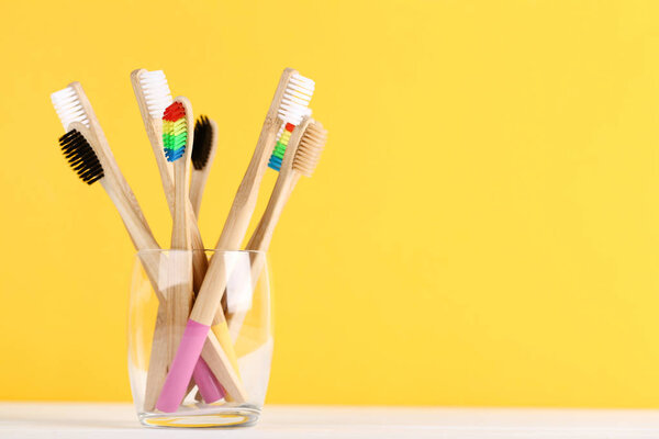 Bamboo toothbrushes in glass on yellow background