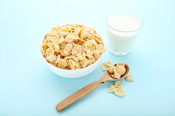 Copos de maíz en tazón con vaso de leche sobre fondo azul —  Fotos de Stock