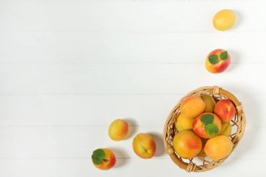 Beyaz ahşap masa üzerinde sepet yeşil yapraklı tatlı kayısı