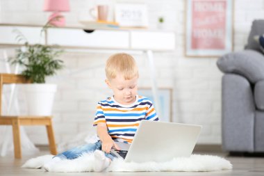 Evde beyaz halı üzerinde oturan dizüstü bilgisayar ile küçük çocuk