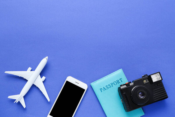 Airplane model with passport, camera and mobile phone on blue background
