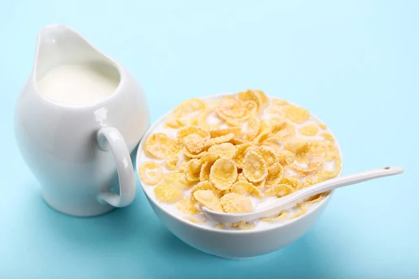 Copos de maíz en tazón con leche y cuchara sobre fondo azul —  Fotos de Stock