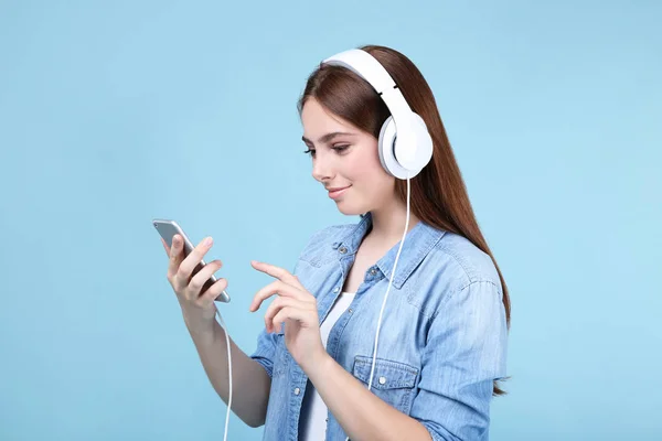 Jonge vrouw met koptelefoon en mobiele telefoon op blauwe achtergrond — Stockfoto