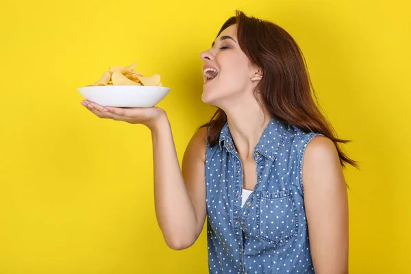 Junge Frau mit Kartoffelchips im Teller auf gelbem Hintergrund — Stockfoto