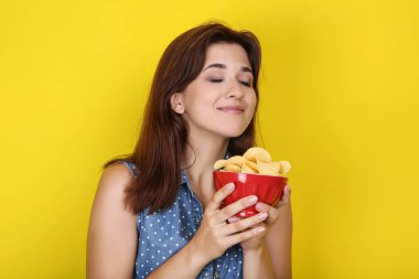 Sarı arka planda kase patates cipsi ile genç kadın