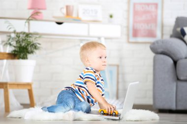 Dizüstü bilgisayar ve araba oyuncak evde oturan küçük çocuk